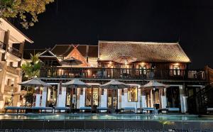 un edificio con mesas y sombrillas frente a una piscina en Buri Sriping Riverside Resort & Spa - SHA Extra Plus, en Chiang Mai