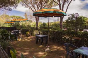 un patio con mesas, sillas y una sombrilla en Area Sosta La Pampa en Marina di Grosseto