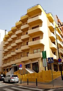 un gran edificio amarillo con coches estacionados frente a él en Hotel Andalucía, en Benidorm