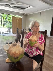 an older woman sitting at a table with a large coconuts at Heidi’s Beach Stay in Mombasa