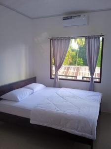 a bedroom with a white bed with a window at Riung Tiga Empat Tujuh Guesthouse in Riung
