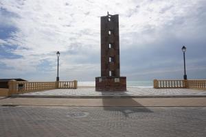 Una torre del reloj en un muelle con el océano detrás. en Rompeolas Playa en Chipiona