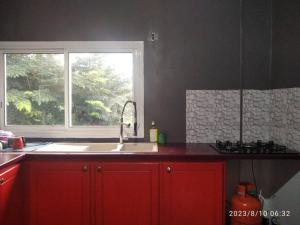 d'une cuisine avec des placards rouges, un évier et une fenêtre. dans l'établissement chambre pour voyageur, à Bouéni