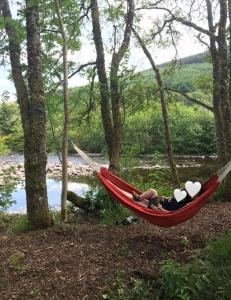 a person laying in a hammock next to a river at River Cottage in Drumnadrochit