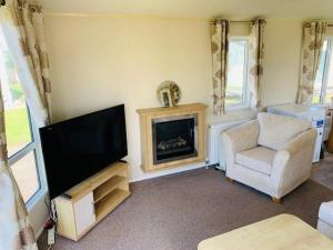 a living room with a flat screen tv and a chair at Newbeach Holiday Park - Greenfields in Dymchurch