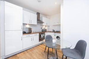 una cocina con armarios blancos y una mesa y sillas de cristal. en Modern 1 BR Apartment Near Shoreditch - 10 Min Walk en Londres