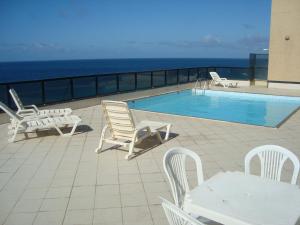 a patio with chairs and a swimming pool with the ocean at Flat na Praia do Farol da Barra in Salvador