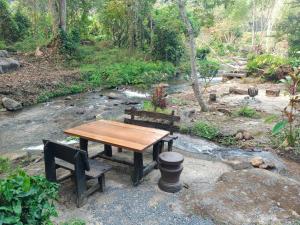 a wooden table and two benches next to a stream at ธารทอง ลอดจ์ Tharnthong Lodge in Ban Pang Champi