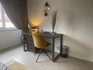 a desk with a yellow chair in a room with a window at Appartamento confortevole in Deinze