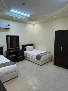 a bedroom with two beds and a dresser and a television at قصر نوماس للشقق المخدومة الواديين in Al Wadeen