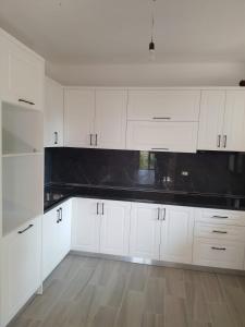 a white kitchen with white cabinets and black counter tops at Appartamento Mërqi in Lezhë