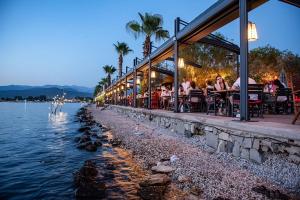 Un restaurante con gente sentada en mesas junto al agua. en Sunset beach club Fethiye 3 bedroom apartment, en Fethiye