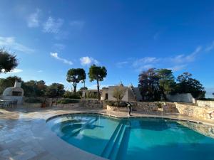 a large swimming pool with a stone wall and blue sky at Trulli Clematis with Pool in Selva di Fasano