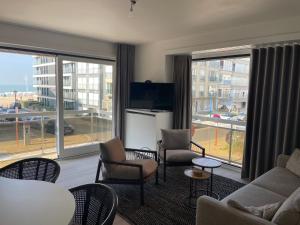 un salon avec un canapé, des chaises et des fenêtres dans l'établissement Dzee Appartement frontaal zeezicht en gratis parking, à Coxyde