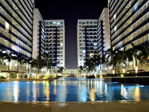 SEA Residences in Pasay near Mall of Asia 2BR and 1BR في مانيلا: مسبح كبير في مدينة في الليل مع مباني طويلة