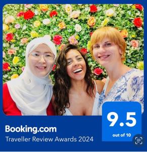 three women standing in front of a wall of flowers at Dreams beach hostel in Dubai