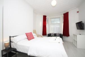 1 dormitorio con cama blanca y cortinas rojas en BARTON BEACHSIDE APARTMENTS - Free Parking, Modern Chic, Central Beach Location, Some Sea Views - Families Couples or Over 23 years en Blackpool