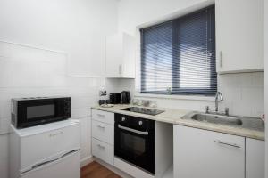 a white kitchen with a sink and a microwave at BARTON BEACHSIDE APARTMENTS - Free Parking, Modern Chic, Central Beach Location, Some Sea Views - Families Couples or Over 23 years in Blackpool