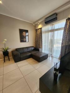 a living room with a leather couch and a large window at 10th floor, Unit 1008, in The Capital Trilogy, overlooking Sun Time Square in Pretoria