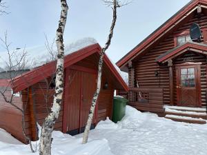 ein Blockhaus im Schnee neben zwei Bäumen in der Unterkunft Koslig tømmerhytte in Kilpisjärvi