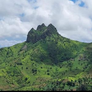 een groene heuvel met een berg op de achtergrond bij Splanada poilon in Assomada