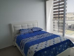 a bedroom with a bed with blue and white sheets and a window at Apartamento Frente al Mar en Puntaroca Sabanilla Atlantico in Sabanilla