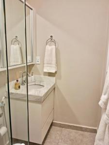 ein weißes Badezimmer mit einem Waschbecken und einem Spiegel in der Unterkunft Loft alto padrão, último andar Uptown c/ garagem in Araçatuba