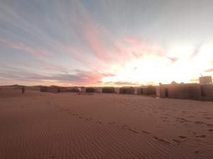 Wüstencamp in Erg Chegaga في Mhamid: غروب الشمس في الصحراء مع وجود شخص يمشي على الرمال