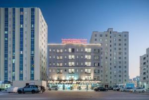 a building in a parking lot with two tall buildings at جوهرة مسقط للشقق الفندقية in Ma‘ābīlah