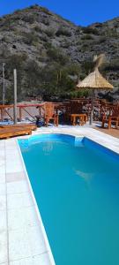 a blue swimming pool with a straw umbrella and chairs at Cabaña Rincón del Sol in Potrerillos