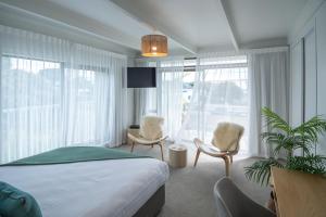 a bedroom with a bed and two chairs and windows at Whispering Sands Beachfront Motel in Gisborne