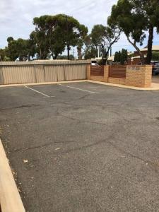 an empty parking lot with a fence and trees at Hyacinth Egan in Kalgoorlie