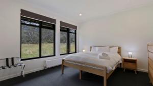 a white bedroom with a bed and two windows at Woodrun in Dinner Plain