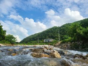 a river with rocks and a house in the background at Danyang Forest 67 in Danyang