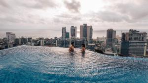 um casal sentado numa piscina de beiral infinito no telhado de um edifício em Cinnamon Red Colombo em Colombo