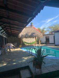 una piscina con una sombrilla de paja y una casa en hotel Las Cabañitas 8873-3748 en Managua