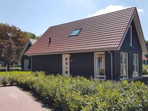 uma casa preta com um telhado castanho e alguns arbustos em Cozy house with a dishwasher in the middle of the Achterhoek em Almen