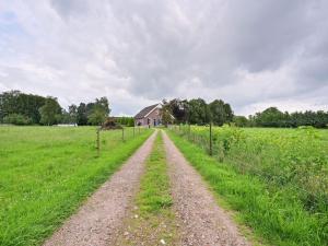 eine unbefestigte Straße auf einem Feld mit einem Haus im Hintergrund in der Unterkunft Farmhouse in De Heurne near the forest in De Heurne