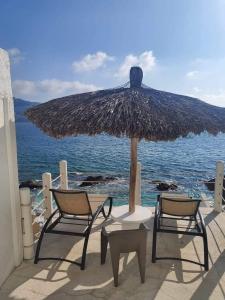 duas cadeiras e um guarda-sol de palha na praia em Hermosa Suite en Acapulco em Acapulco