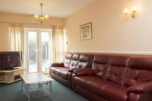 a living room with a brown leather couch and a tv at Southend Guest House - Close to Beach, Train Station & Southend Airport in Southend-on-Sea