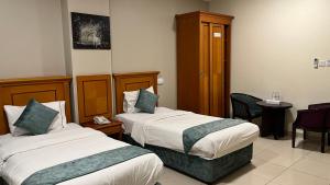 a hotel room with two beds and a chair at Al Murooj Hotel Apartments in Muscat