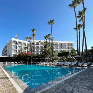 a hotel with a swimming pool with chairs and palm trees at Veronica Hotel in Paphos City