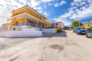 een geel en wit huis met auto's geparkeerd op een parkeerplaats bij Villa Lina in Castelsardo