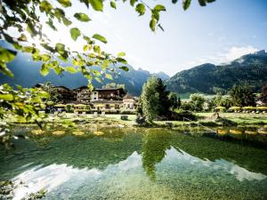 a lake with a house and mountains in the background at Forster's Naturresort in Neustift im Stubaital