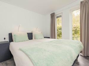 een witte slaapkamer met een groot bed met groene kussens bij Cozy chalet with garden at the edge of the forest in Rijssen