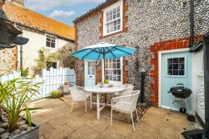 a patio with a table with a blue umbrella at Yew Tree Cottage in Blakeney