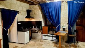 cocina con cortinas azules, mesa y fregadero en Évasion ACCES PMR en Les Roches-lʼÉvêque