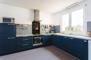 a large kitchen with blue cabinets and a window at Maison Boyardville Piscine Chauffée in Saint-Georges-dʼOléron