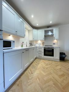 a white kitchen with white cabinets and a wooden floor at Chic Haven in Barnsley in Barnsley