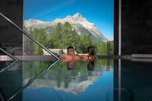 a man and a woman sitting in a swimming pool with a mountain at Nira Alpina in Silvaplana